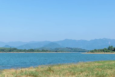 Gölün karşısında bir dağ, kıyıda ise bir çayır var.