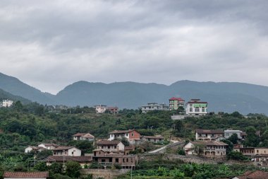 Yağmurdan sonra kırsal alan, bulutlar, yeşil ağaçlar, yeşil dağlar ve evler.