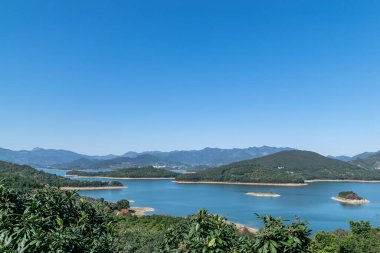 Gölün kıyısı yeşildir, merkezinde bazı küçük adalar vardır, ve gökyüzü ve su mavidir.