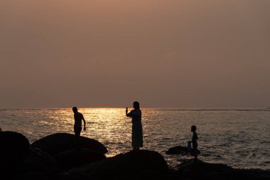 Batan güneşin altındaki kumsal altın rengidir ve sahilde oynayan insanlar bir siluet bırakır.