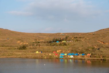Otlaktaki gölde insanlar göl kenarında çadır kurdular.;