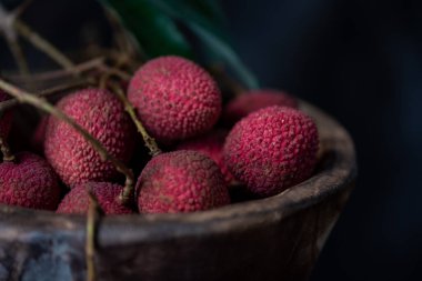 Litchi, ahşap bir tabağa konur, soyulmuş ya da açılmamış, koyu bir ahşap tahıl masasında.