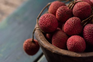 Litchi, ahşap bir tabağa konur, soyulmuş ya da açılmamış, koyu bir ahşap tahıl masasında.
