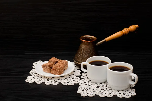 Two cups of coffee on the lace napkins, pots and chocolate turkish dessert on a black background — Stock Photo, Image