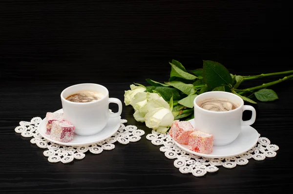 Coffee for two with oriental sweets, a bouquet of white roses on a black background