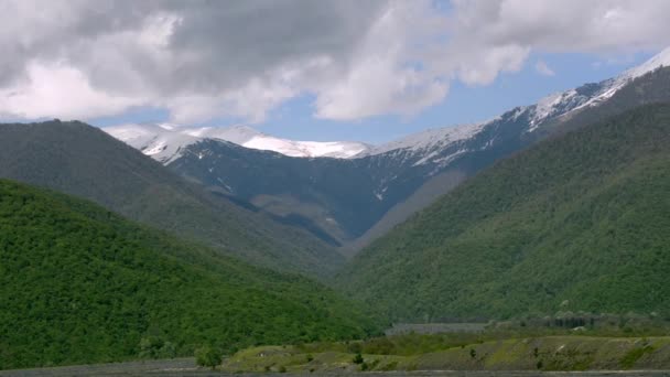 The green slopes of the mountains, snow-capped peaks, dark river flowing below. Spring, Georgia — Stock Video