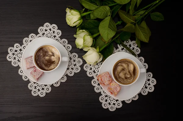 Draufsicht auf zwei Tassen Kaffee mit Milch, türkisches Vergnügen auf einer Untertasse, weiße Rosen. schwarzer Hintergrund — Stockfoto