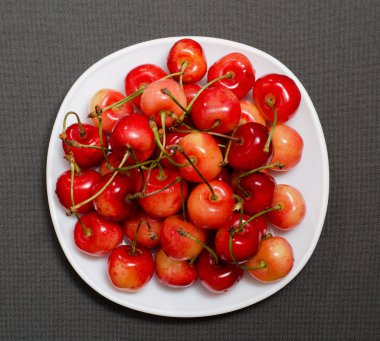 Sarı ve kırmızı kiraz bir plaka, dokulu gri arka plan, üstten görünüm