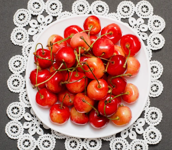 Gul og rød kirsebær i en tallerken på en blondetut. – stockfoto