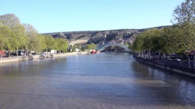 Kura Nehri manzarası, barışın cam köprüsü ve teleferik. Nehrin her iki tarafında ki arabaların hareketi. Tiflis