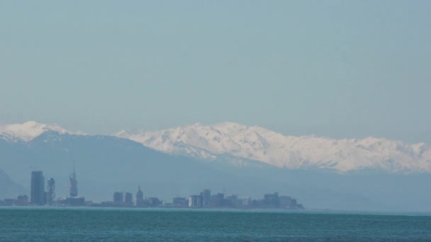 Blick vom Meer auf die Stadt Batumi im Dunst vor schneebedeckten Bergen und wolkenlosem Himmel. Georgien. — Stockvideo