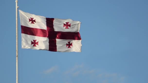 Ondeando la bandera de Georgia en un asta de la bandera contra un cielo azul — Vídeos de Stock