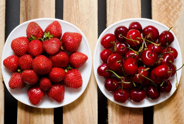 Strawberries and cherries in a plate on a wooden background, top view — Stock Photo, Image