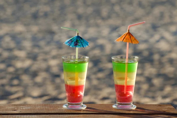 Multi-colored cocktails on a wooden table on the beach, the sand on the background