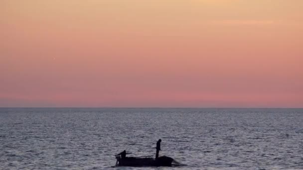 在落日的天空背景上的一条船上的渔民撒网入海 — 图库视频影像