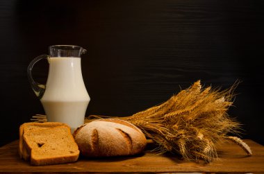 Süt, çavdar ekmeği ve bir demet, bir siyah arka plan, metin için yer ile bir sürahi ile ahşap masa