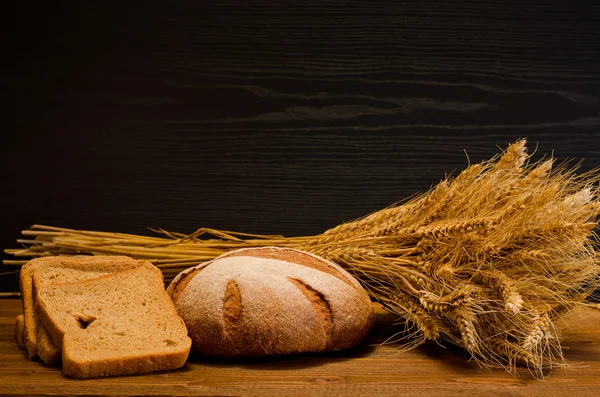 Круглый и квадратный ржаной хлеб, сноп на деревянном столе, черный фон, место для текста — стоковое фото