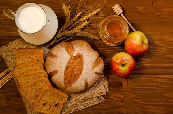 Кувшин с молоком, шипы, ржаной хлеб, мед и яблоки на деревянном столе, вид сверху, место для текста — стоковое фото
