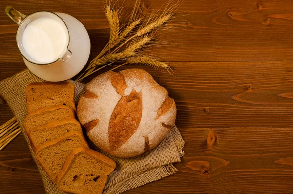Кувшин с молоком, круглый и квадратный ржаной хлеб и уши на деревянном столе, вид сверху, место для текста — стоковое фото