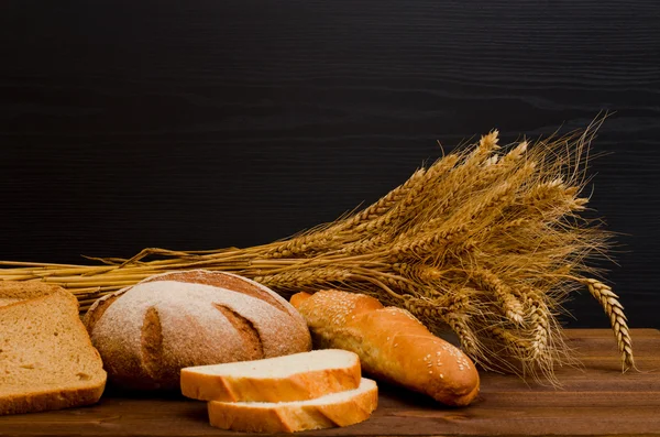 Белый и ржаной хлеб, буханка, сноп на деревянном столе, черный фон, место для текста — стоковое фото
