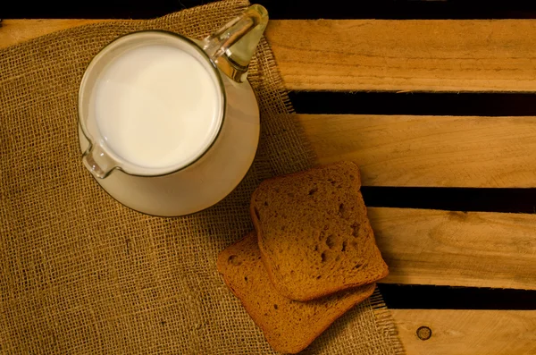 Jug of milk and a piece of rye bread on a sacking, a top view — Stock Photo, Image