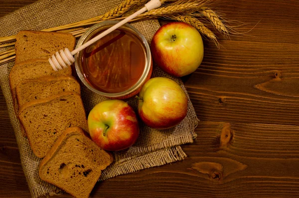 Frasco de mel, maçãs, pão de centeio, orelhas em sacos, mesa de madeira, vista superior — Fotografia de Stock