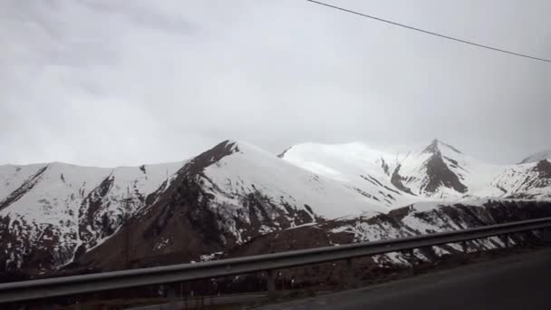 Pohled na zasněžené vrcholky hor proti obloze, zakryté mraky. Na silnici. Gruzie, Kavkaz. — Stock video