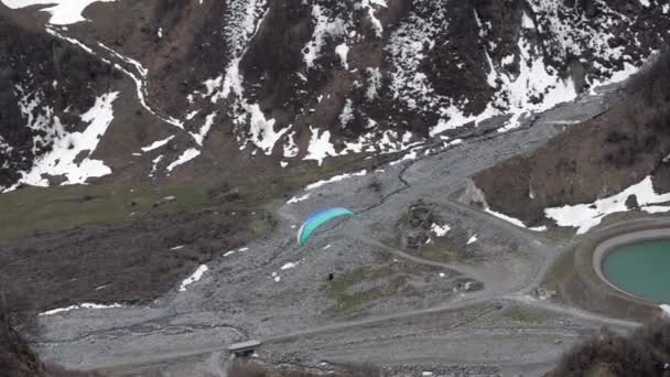 Paraglider naar beneden tegen de achtergrond van het mooie meer en de besneeuwde heuvels. Georgia, Caucasus. — Stockvideo
