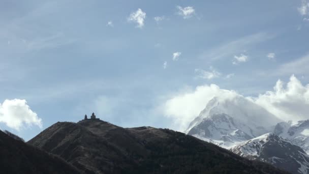 Nézd, a templom a Szent Háromság Gergeti a háttérben lebegő felhők és a Mount Kazbek — Stock videók