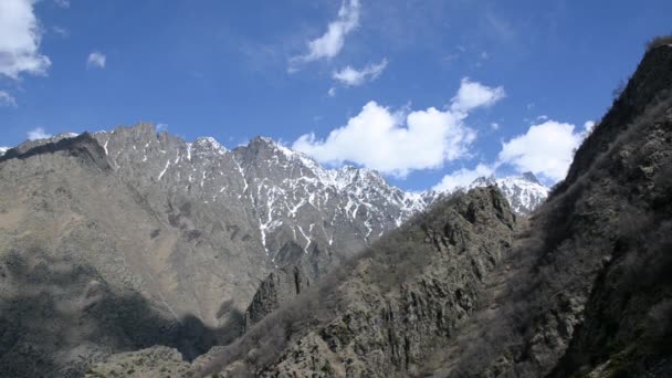 Leicht weiße Wolken schweben über dem Gipfel eines hohen, zerklüfteten Gebirges mit Schneeresten. Kaukasus. Georgien. — Stockvideo