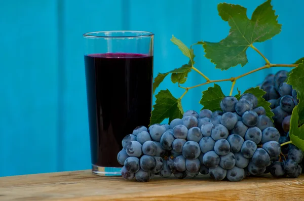 Uvas e um copo de suco em um fundo azul — Fotografia de Stock