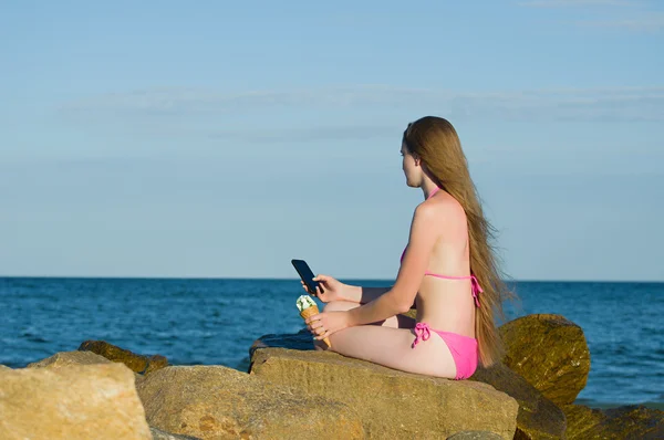 Дівчина задумливо дивиться в телефон, в купальнику на пляжі — стокове фото