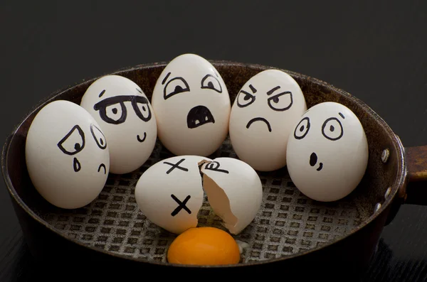 Huevo roto en una sartén rodeado de huevos enteros con diferentes emociones — Foto de Stock