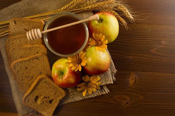 Спелые яблоки, банка меда, ржаной хлеб, уши и желтая маргаритка на мешковине — стоковое фото