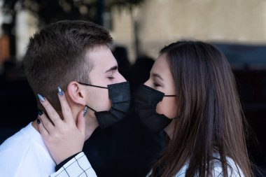 Cerrahi maskelerle öpüşen genç bir çift. Virüs enfeksiyonu korkusu. Karantina salgını COVID.