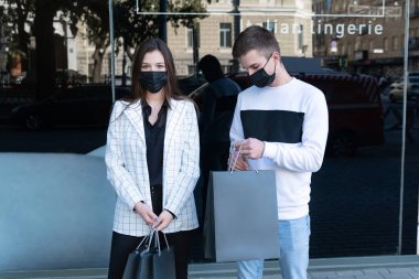 Yüzü maskeli genç bir çift ellerinde alışveriş malzemesi var. Kara Cuma alışverişi.