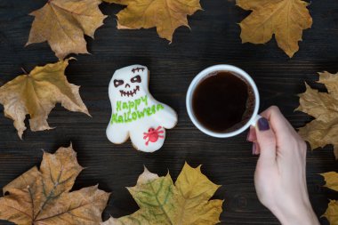 Ahşap arka planda bir fincan kahveyi tutan kadın. Güz kompozisyonu kuru yapraklar ve bir hayalet gibi zencefilli ekmek..