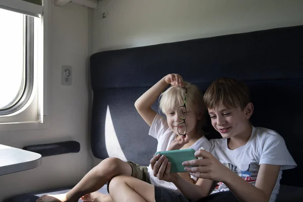 Two brothers in compartment carriage gaming at smartphone. Entertaining children during trip. Travel by railway