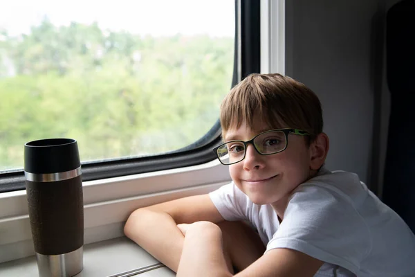 小学生が電車に乗っている 眼鏡をかけた少年が電車の中でテーブルに座っている 鉄道旅行 — ストック写真