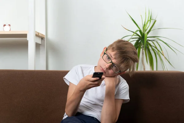 Bored boy with glasses switches TV channels. Child is watching TV