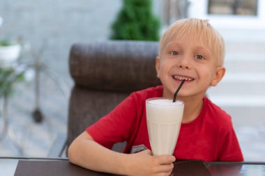 Sarışın çocuk milkshake içiyor ve gülümsüyor. Kafedeki çocuk.