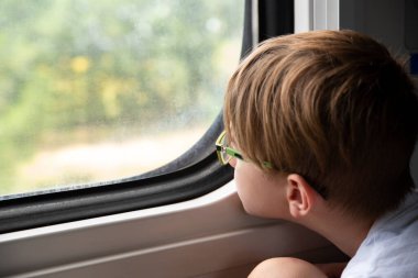 Çocuk düşünceli bir şekilde tren penceresinden dışarı bakıyor. Çocuklarla birlikte trenle seyahat etmek. Demiryolu ile seyahat et..