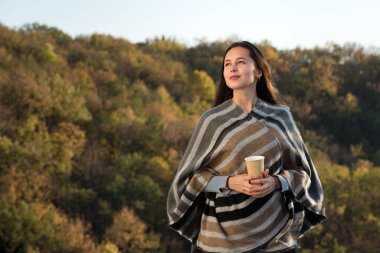 Doğada kahve içen tatlı bir kız. Kadın dikkatli bir şekilde uzaklığa bakıyor.