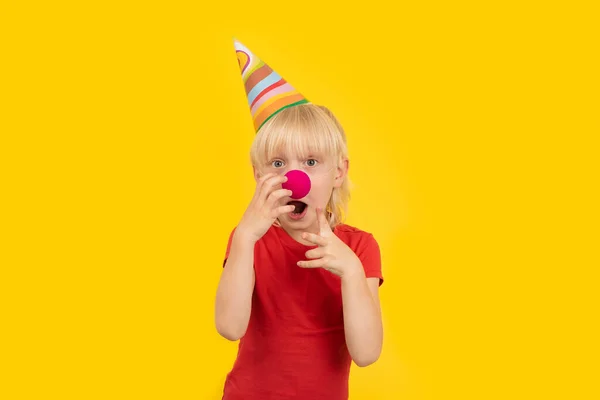 Überraschter Blonder Junge Mit Clownsnase Und Partymütze Auf Gelbem Hintergrund — Stockfoto