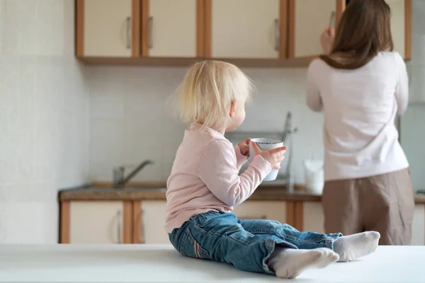 Mom and two-year-old baby with cup in their hands in kitchen