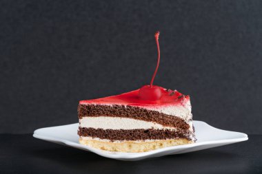 Beyaz tabakta kirazlı bisküvi keki. Siyah arkaplan.