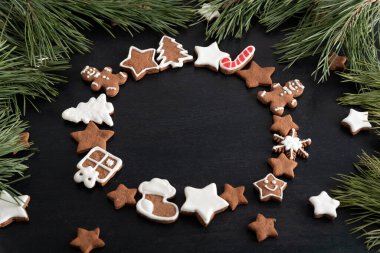 Siyah arka planda çember şeklinde zencefilli kurabiye, ladin dalları. Boşluğu kopyala