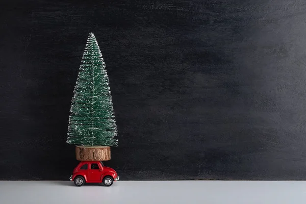Small artificial tree on roof of toy car on black background. Christmas tree delivery. Copy space.