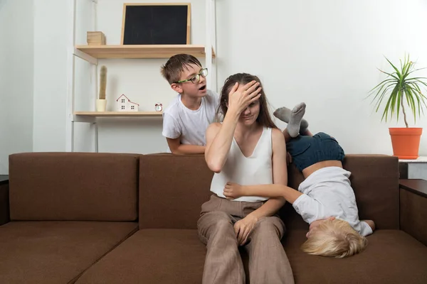 Nanny for two wild children. Mom holds her forehead with her hand against crazy little kids.