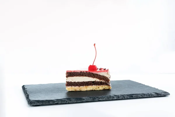 Piece of layered cake with maraschino cherry. Side view to piece of cake on white background.